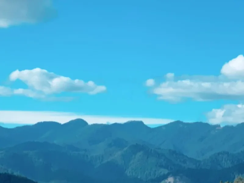 Big white clouds in a blue sky above layered forested mountain ridges
