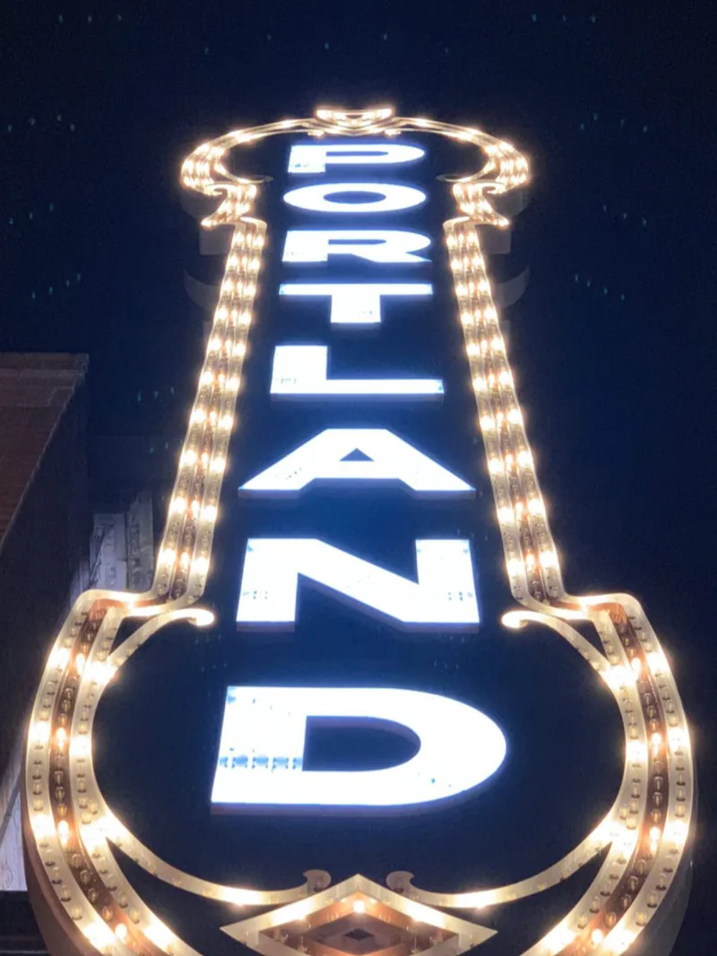 Vertical PORTLAND marquee sign lit with rows of bulbs against a dark night sky