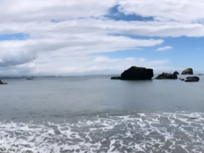 Low surf rolling onto a sandy beach with sea stacks offshore and white clouds overhead