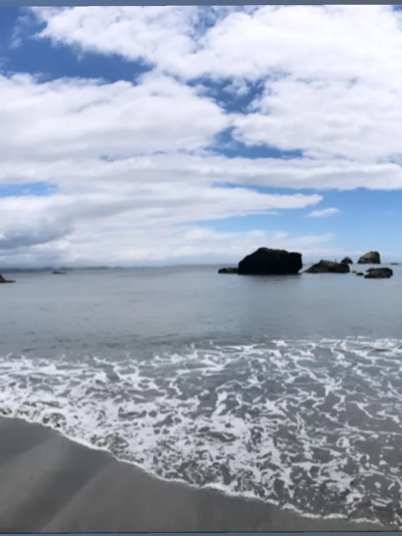 Low surf rolling onto a sandy beach with sea stacks offshore and white clouds overhead