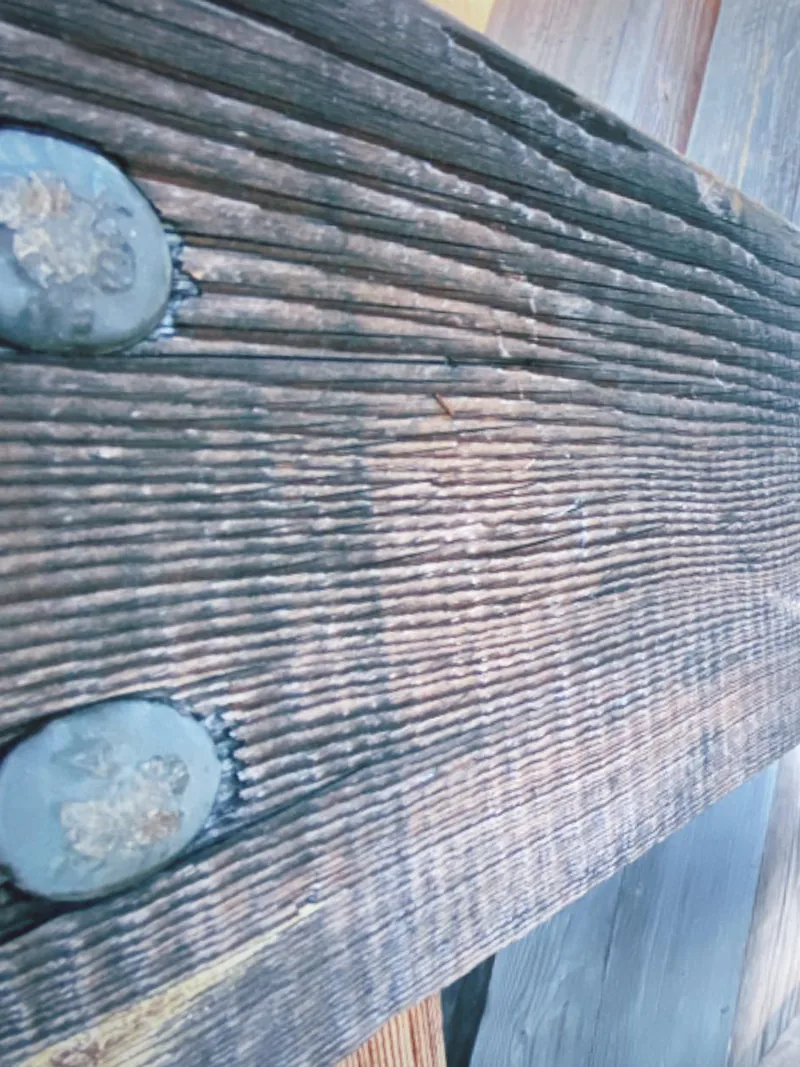 Weathered covered bridge timber rail with bolts Close view of a weathered wooden rail held by round iron bolts inside a covered bridge