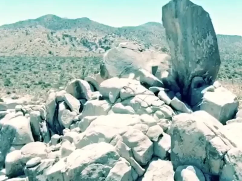 A pile of pale granite boulders on a desert ridge under a pale blue sky