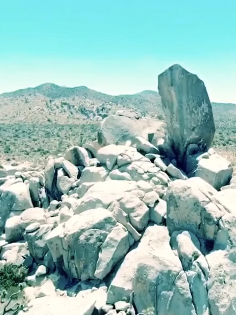 A pile of pale granite boulders on a desert ridge under a pale blue sky