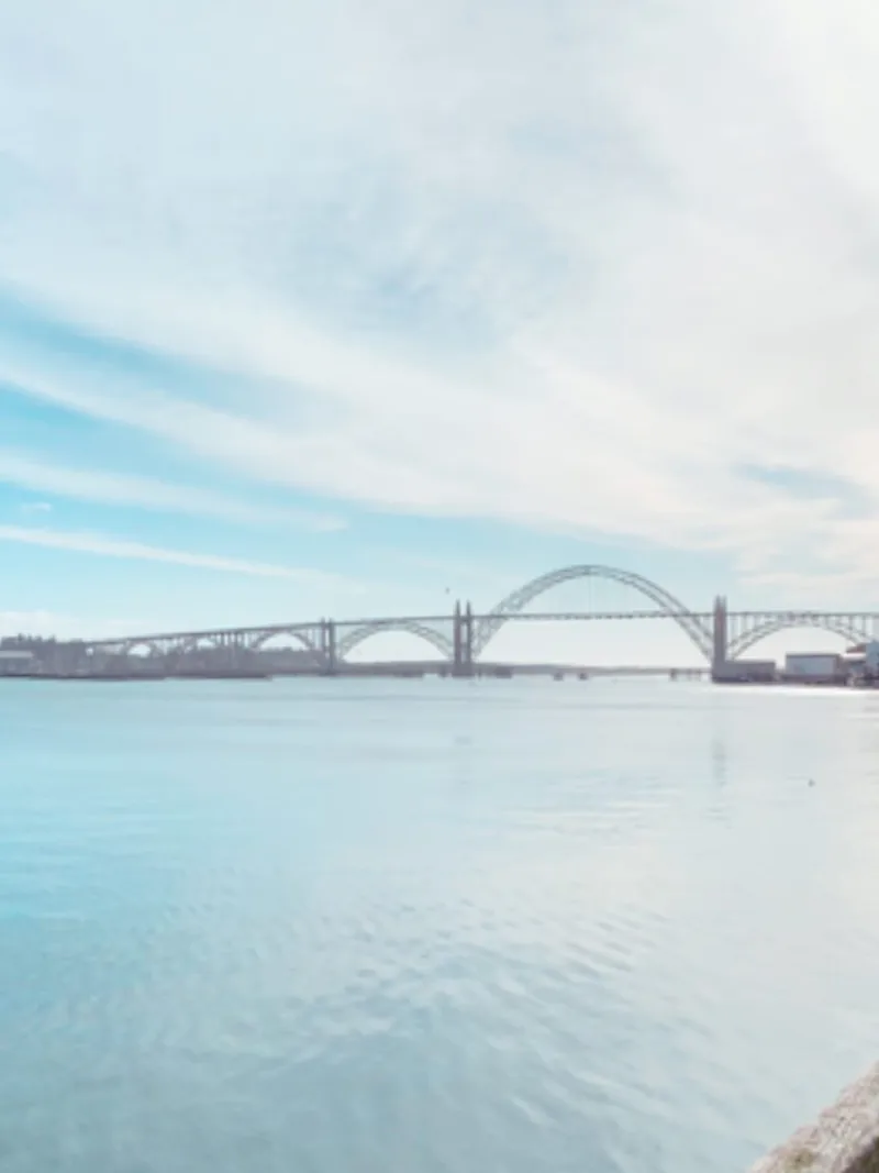 The Yaquina Bay Bridge arching across a calm blue Yaquina Bay in Newport, Oregon, under a wide streaked sky